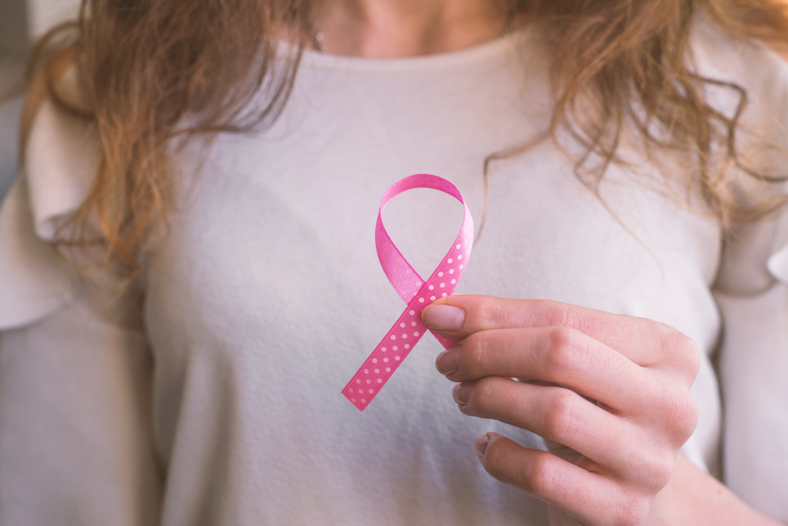 Woman holding a pink breast cancer ribbon after breast reconstructive surgery using microsurgery techniques