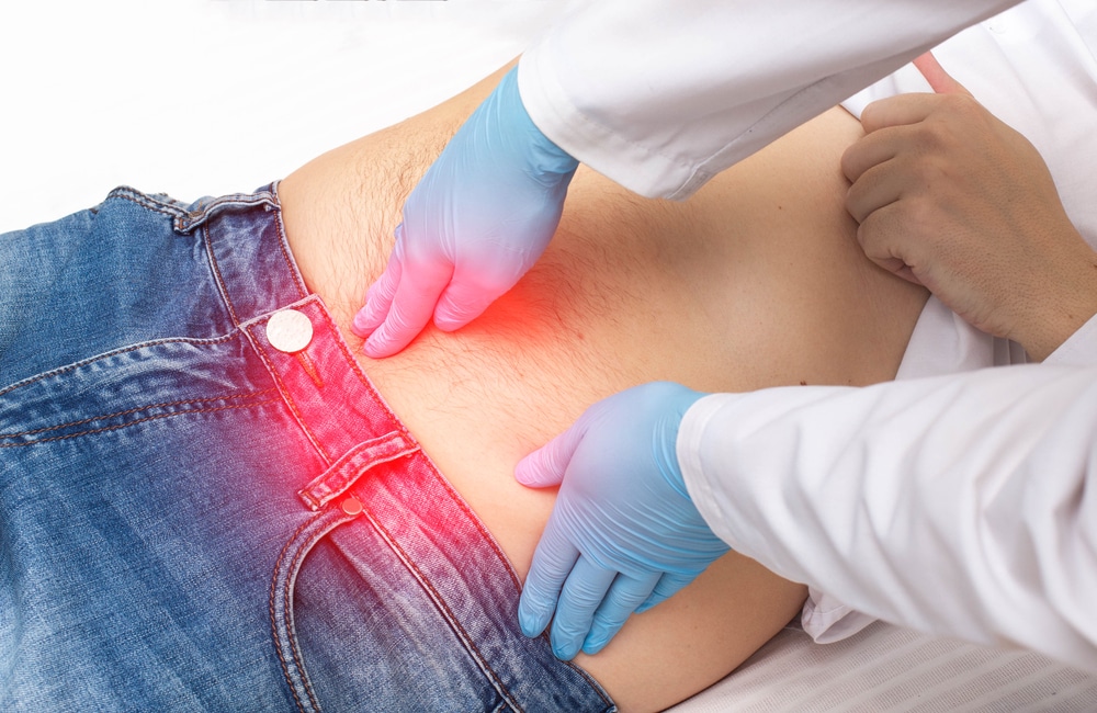 A doctor's gloved hand examines a man's navel area for a suspected umbilical hernia